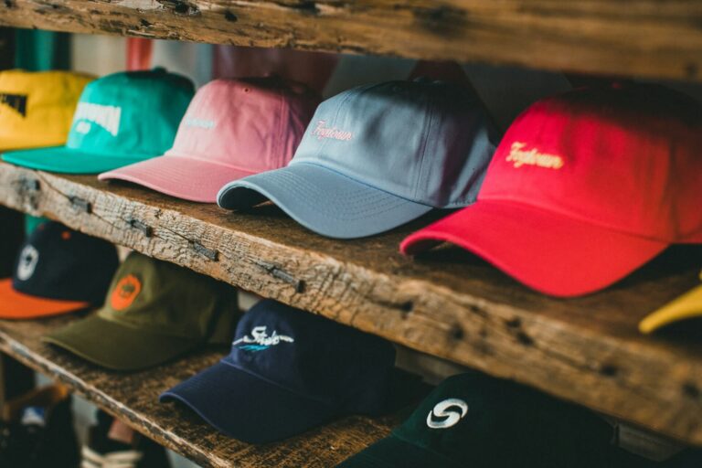 A row of colorful baseball caps on wooden shelves, featuring vibrant red, blue, pink, and green hues.