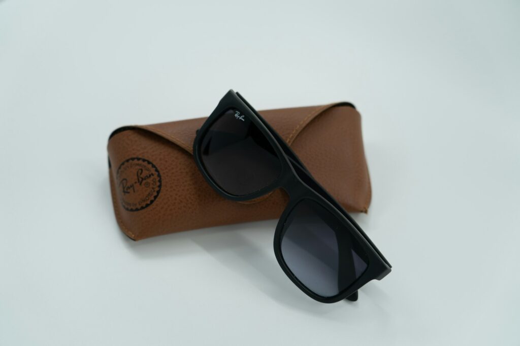 Sleek black Ray-Ban sunglasses with dark lenses are placed at an angle on a textured brown leather case.