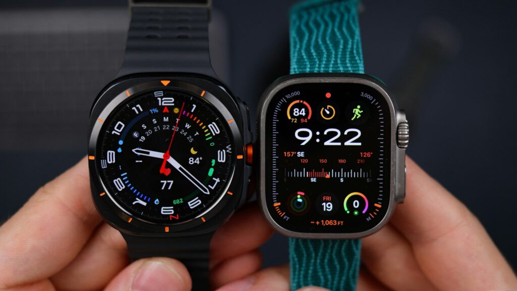 Two smartwatches are held side by side. The left watch has a black strap and circular face displaying analog time. The right has a blue strap and digital interface.