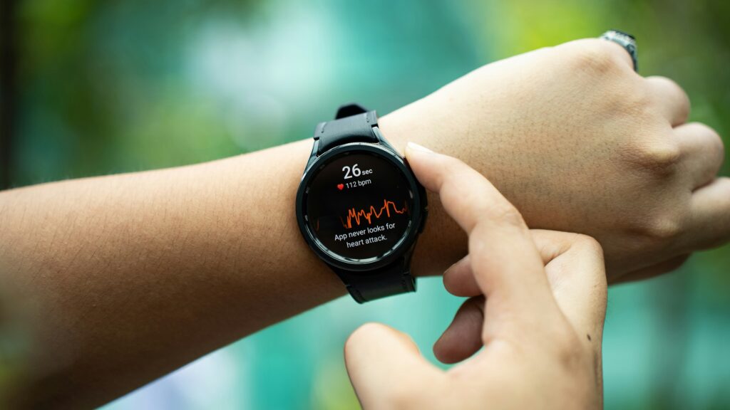 Close-up of a person's wrist wearing a smartwatch displaying heart rate data and an ECG graph, with fingers interacting with the screen; green blurred background.