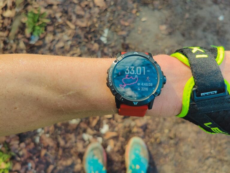 Close-up of an arm wearing a smartwatch displaying 33.01 km distance. The background shows a dirt path, suggesting an outdoor run.