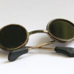 Vintage round sunglasses with black lenses and thin metal frames rest on a white surface.