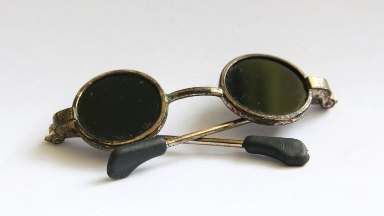 Vintage round sunglasses with black lenses and thin metal frames rest on a white surface.