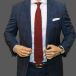 Man in a blue plaid suit and white shirt wearing a red tie showing the perfect tie length.
