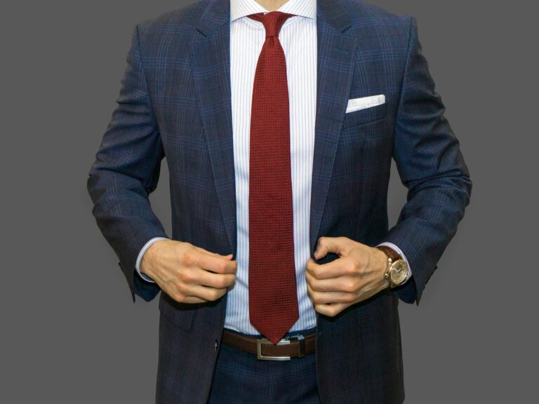 Man in a blue plaid suit and white shirt wearing a red tie showing the perfect tie length.