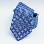 A neatly folded blue necktie with a pattern of small white squares rests against a white background.