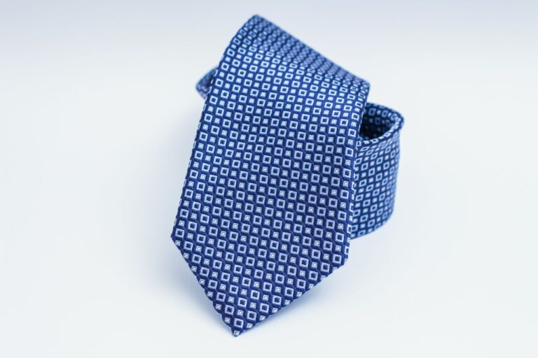 A neatly folded blue necktie with a pattern of small white squares rests against a white background.
