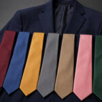 Seven solid-colored neckties are arranged on a dark navy suit jacket, featuring shades of red, blue, yellow, gray, brown, pink, and green.